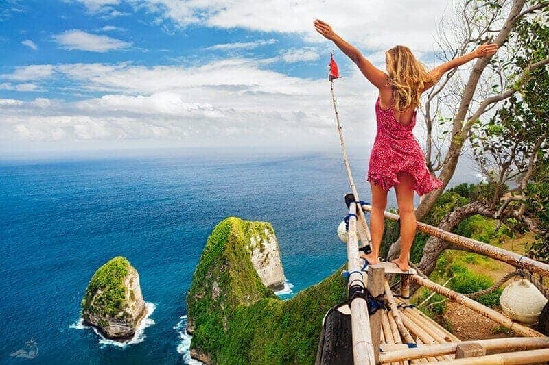 Kelingking, Nusa Penida — wisatawan berdiri di perahu bambu 'Titanic shipwreck' menghadap tebing T-Rex dan laut biru (2017)