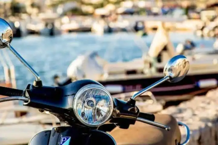 Close-up view of a black scooter parked near the harbor with boats on the water in Sanur Bali &ndash; GoTravela Motorbike Rental