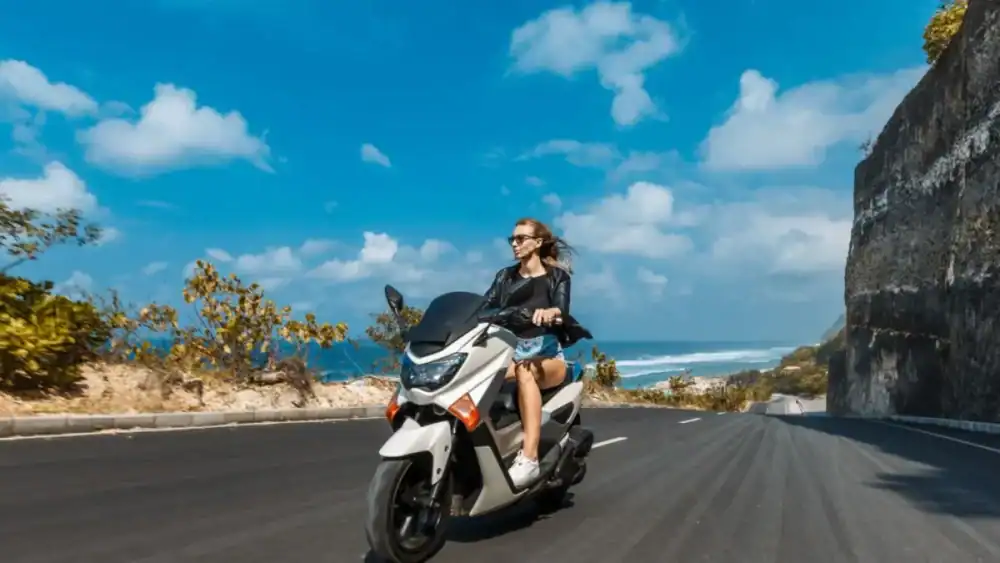 Wisatawan perempuan berkendara motor di jalan tepi tebing Pantai Melasti Bali