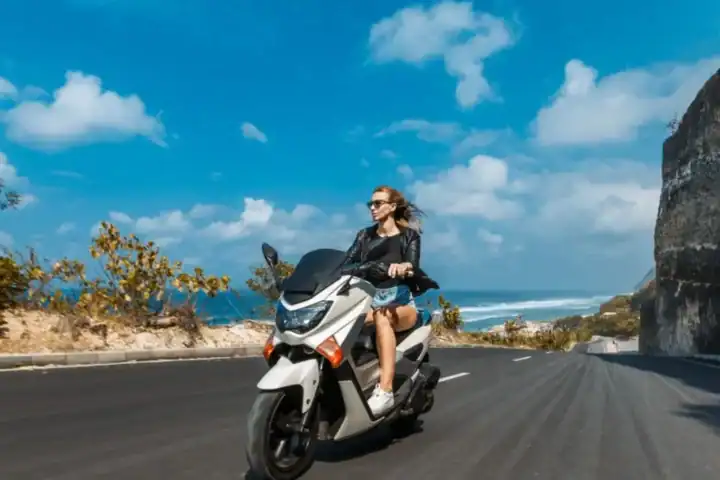 Wisatawan perempuan berkendara motor di jalan tepi tebing Pantai Melasti Bali
