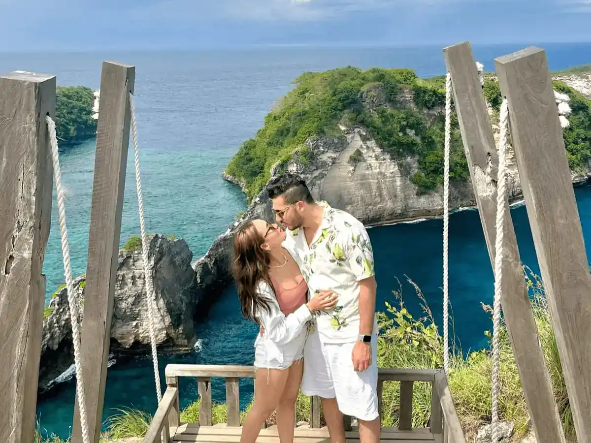 Pasangan berciuman di Rumah Pohon Molenteng (Raja Lima), tebing karst dan laut biru Nusa Penida.