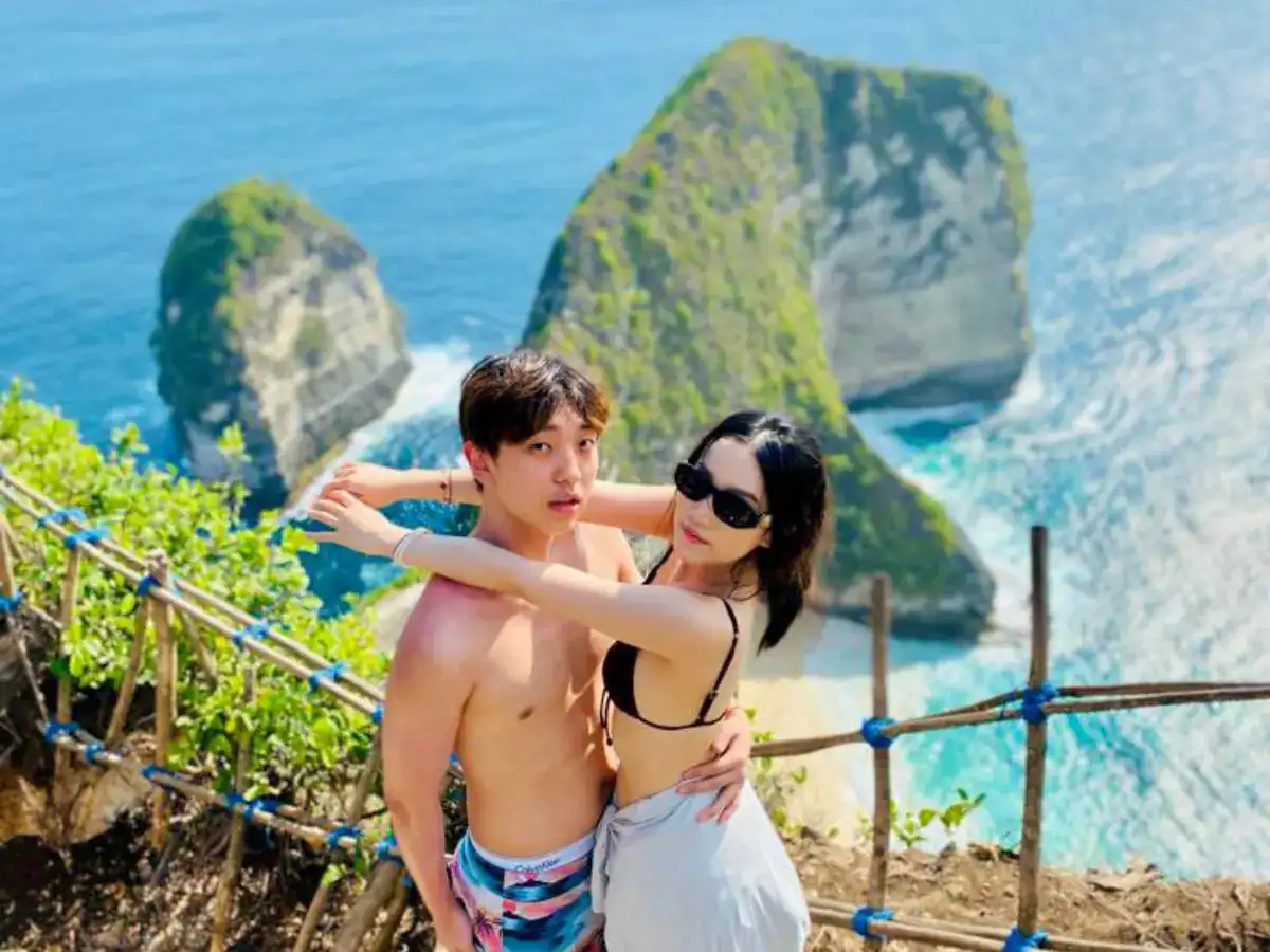 Pasangan berpose di viewpoint Kelingking Beach (T-Rex), tebing hijau dan laut turquoise Nusa Penida.