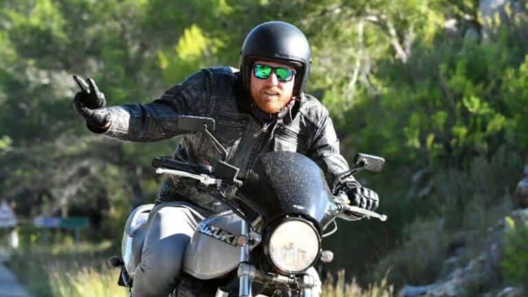 Man riding a black motorcycle wearing helmet and sunglasses on a road surrounded by greenery in Jimbaran Bali – GoTravela Indonesia