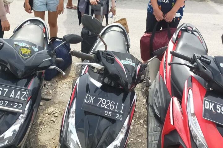 Row of rental scooters parked on a rocky roadside with tourists standing behind in Nusa Penida Bali &ndash; GoTravela Indonesia