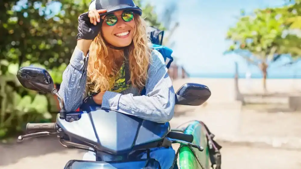 traveler perempuan tersenyum duduk di atas skuter di Bali dengan suasana pantai